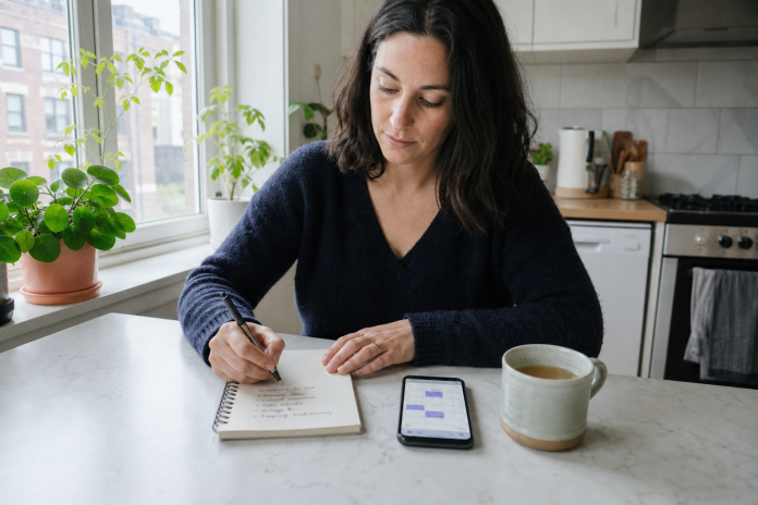 Preparing questions before a psychic reading Woman writing a list of questions in a notebook at a kitchen table before a phone psychic reading