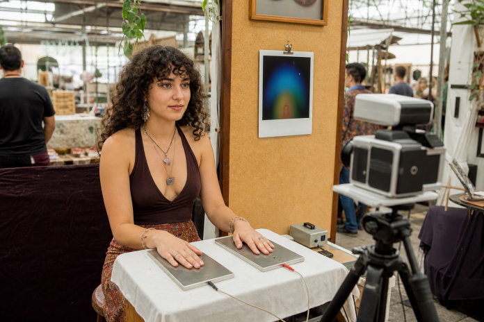 What is your aura: an aura photography booth Young woman with her hands on sensor plates at an aura photography booth at a craft market