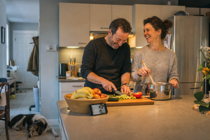 Signs of a good relationship: an ordinary evening Couple laughing while cooking dinner together in an ordinary kitchen